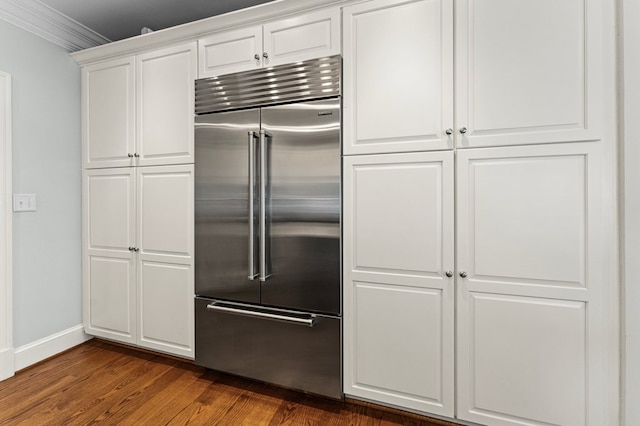 kitchen with white cabinets, ornamental molding, built in refrigerator, and dark wood-type flooring