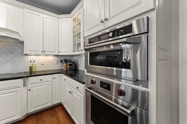 kitchen with white cabinets, decorative backsplash, premium range hood, and oven