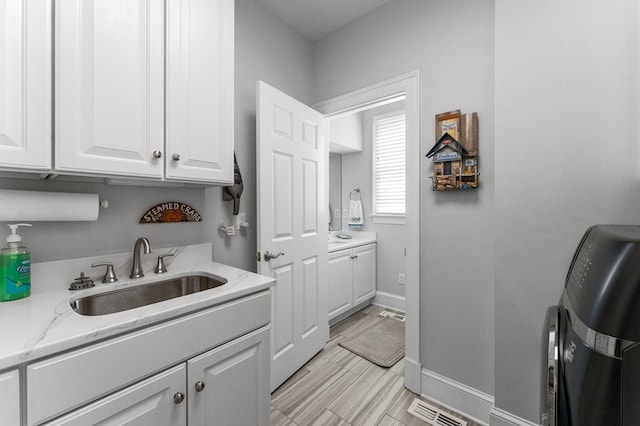 kitchen with white cabinetry, sink, and light stone counters