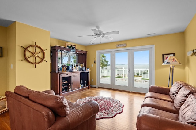 living room featuring ceiling fan, a water view, light wood-type flooring, and indoor bar