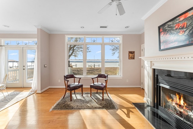 living area with light wood finished floors, visible vents, baseboards, a fireplace with flush hearth, and ornamental molding