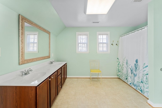 bathroom featuring visible vents, baseboards, vaulted ceiling, double vanity, and a sink