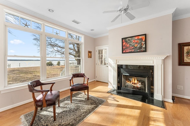 living area with visible vents, crown molding, baseboards, a fireplace with flush hearth, and light wood-type flooring