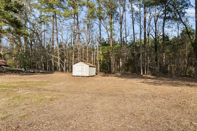 view of yard featuring a forest view, a storage shed, and an outdoor structure