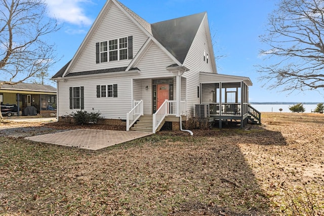 view of front of house featuring a patio, central AC unit, roof with shingles, a sunroom, and a water view