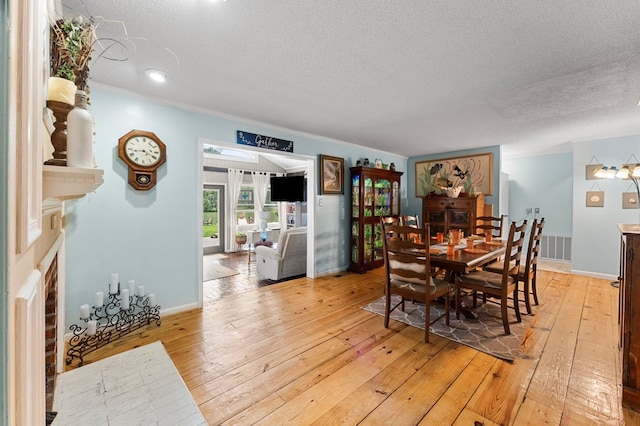 844 Monarch Shores Rd, Kilmarnock, VA 22482 - dining room with light wood-style flooring, a textured ceiling, a fireplace, ornamental molding, and baseboards