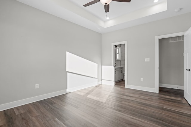 empty room featuring dark wood-type flooring, a raised ceiling, and ceiling fan