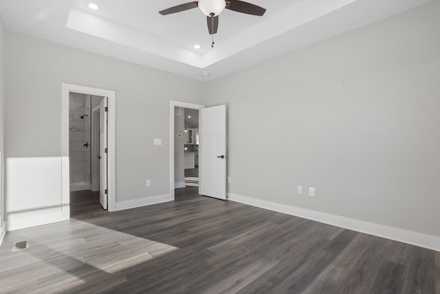 unfurnished bedroom with dark wood-type flooring, ceiling fan, ensuite bathroom, and a tray ceiling