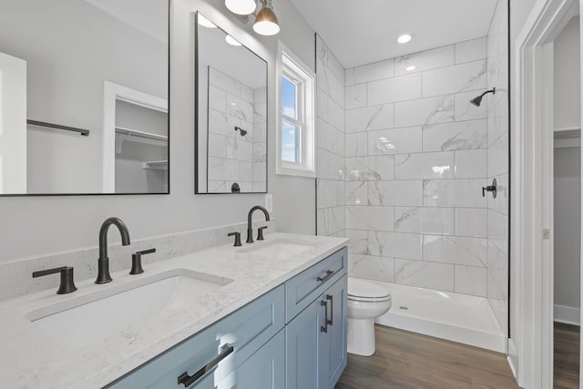 bathroom featuring toilet, vanity, wood-type flooring, and a tile shower