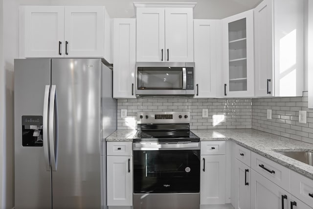 kitchen with stainless steel appliances, white cabinets, tasteful backsplash, and light stone countertops