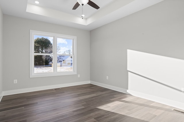 spare room with dark wood-type flooring, ceiling fan, and a tray ceiling