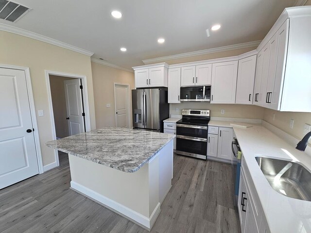 kitchen featuring sink, appliances with stainless steel finishes, white cabinetry, a center island, and light stone countertops