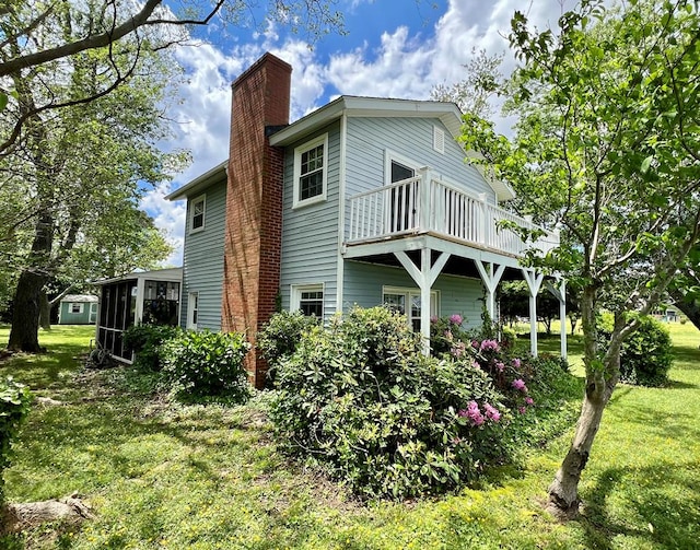 view of property exterior featuring a chimney, a yard, a sunroom, and a balcony