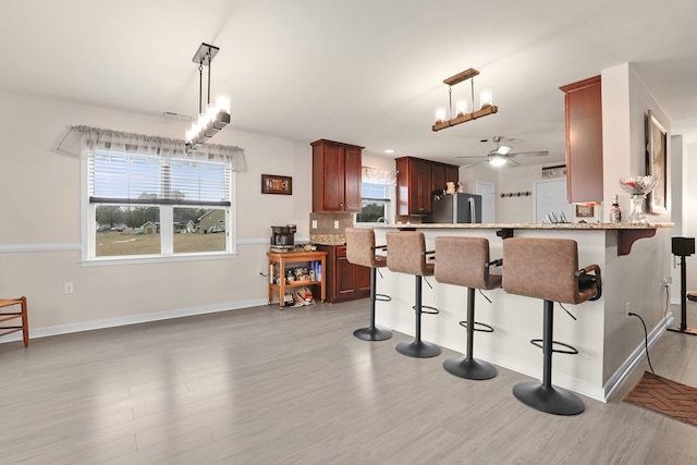 kitchen with a breakfast bar, a ceiling fan, light wood-style floors, freestanding refrigerator, and decorative backsplash