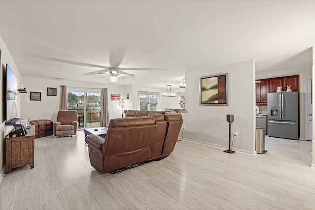 living room featuring ceiling fan with notable chandelier, light wood-type flooring, and baseboards