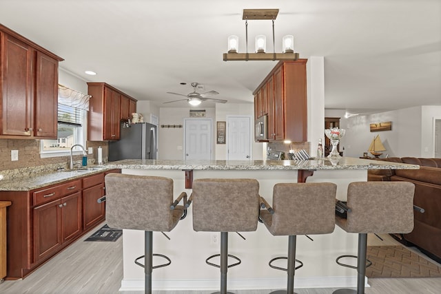 kitchen with backsplash, appliances with stainless steel finishes, open floor plan, a sink, and light stone countertops