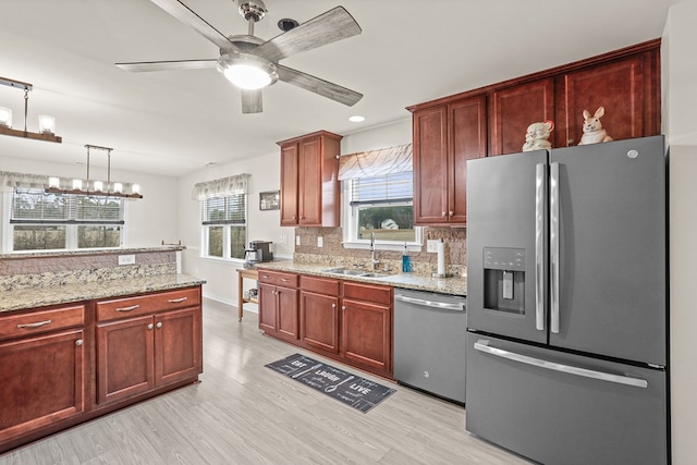 kitchen with light stone counters, a sink, light wood-style floors, appliances with stainless steel finishes, and decorative backsplash