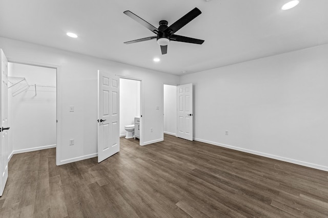 unfurnished bedroom featuring dark wood-type flooring, ensuite bath, ceiling fan, a spacious closet, and a closet