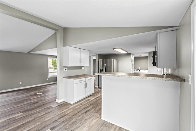 kitchen featuring white cabinetry, stainless steel fridge with ice dispenser, lofted ceiling, and kitchen peninsula