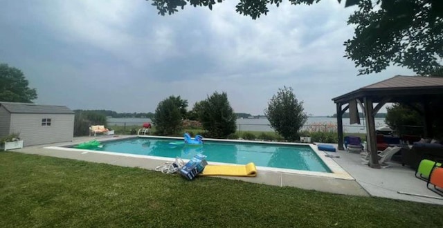 pool with an outbuilding, a water view, a lawn, a gazebo, and a shed