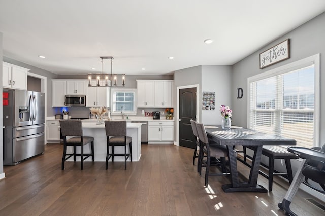 kitchen featuring hanging light fixtures, stainless steel appliances, white cabinets, and a kitchen island with sink