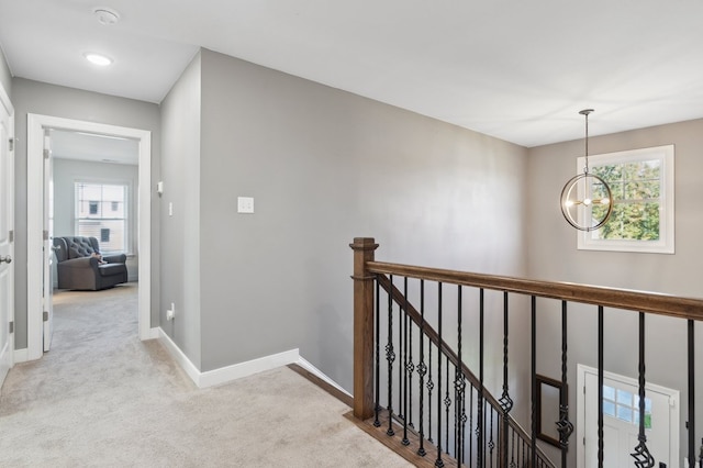 hallway featuring light colored carpet and a notable chandelier