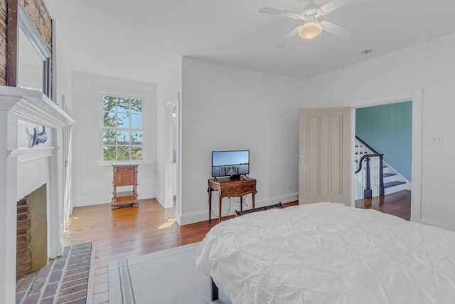 bedroom with hardwood / wood-style flooring, ceiling fan, and a fireplace