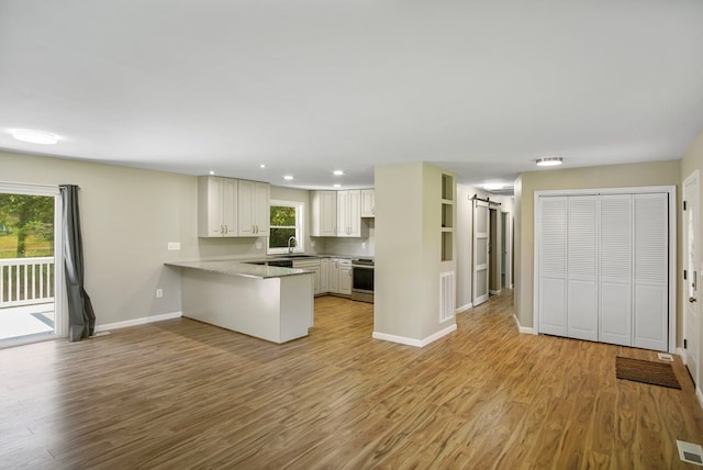 kitchen featuring white cabinetry, stainless steel range, a barn door, kitchen peninsula, and light hardwood / wood-style floors