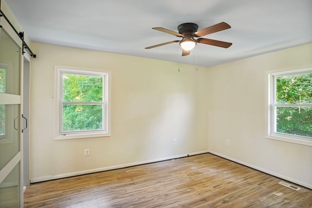 unfurnished room with ceiling fan, a barn door, light wood-type flooring, and a wealth of natural light