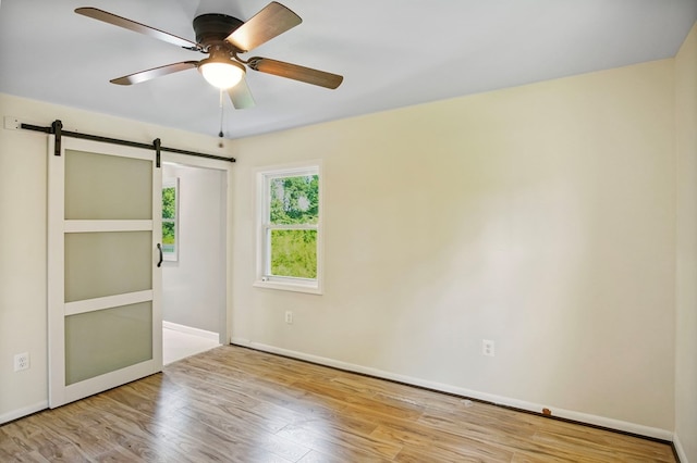 unfurnished bedroom featuring light wood-type flooring, a barn door, and ceiling fan