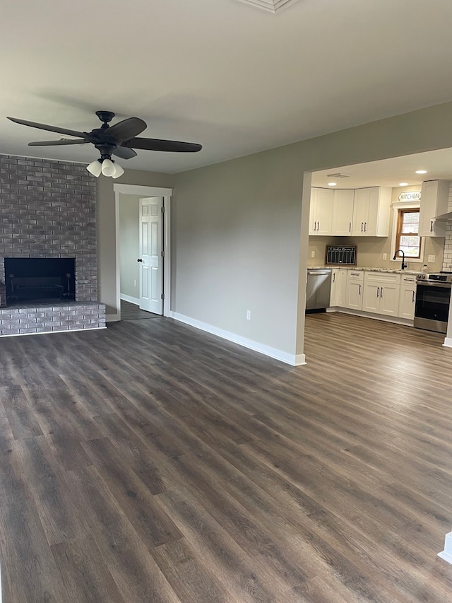 unfurnished living room with a brick fireplace, sink, dark wood-type flooring, and ceiling fan