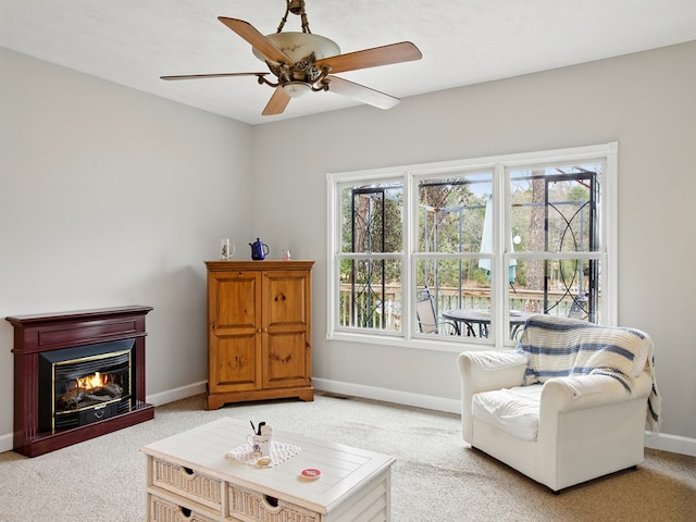 living area with a glass covered fireplace, baseboards, a healthy amount of sunlight, and ceiling fan