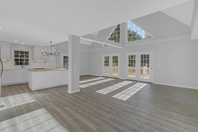 unfurnished living room featuring sink, high vaulted ceiling, light wood-type flooring, and a notable chandelier