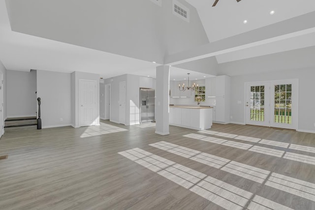 unfurnished living room featuring light hardwood / wood-style flooring, high vaulted ceiling, and ceiling fan with notable chandelier