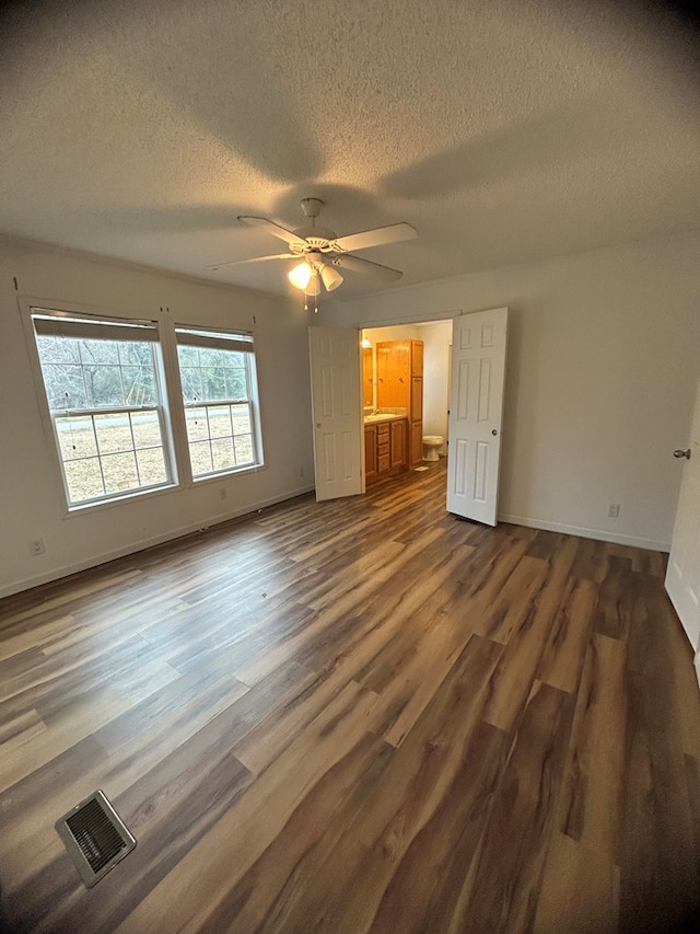 unfurnished bedroom with a textured ceiling, ceiling fan, dark wood-type flooring, and connected bathroom