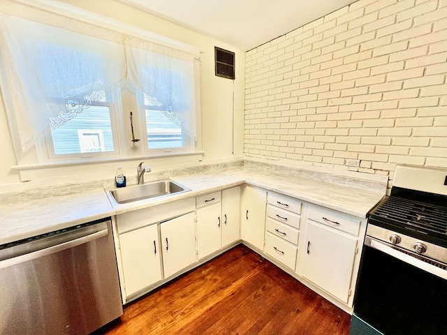 kitchen with brick wall, stainless steel appliances, sink, dark hardwood / wood-style floors, and white cabinetry