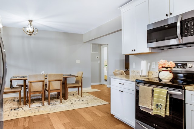 kitchen featuring appliances with stainless steel finishes, white cabinetry, light wood finished floors, and light stone counters