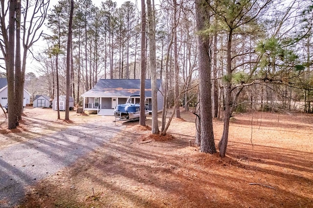 view of front of property with a storage shed, driveway, covered porch, and an outbuilding