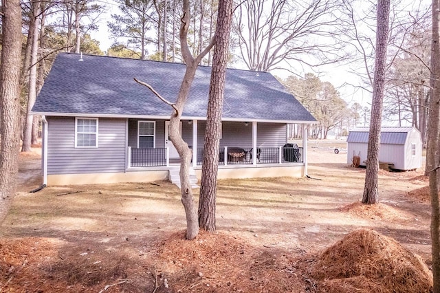 view of front of home featuring a storage shed, a porch, roof with shingles, and an outdoor structure