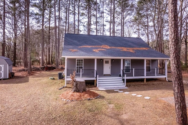 view of front of property featuring covered porch, central AC, a storage shed, and roof with shingles