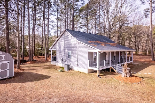 view of side of home featuring an outbuilding, cooling unit, covered porch, a shingled roof, and a storage unit