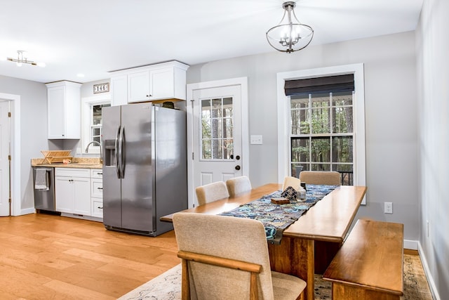 dining area with light wood-style floors, plenty of natural light, baseboards, and a notable chandelier