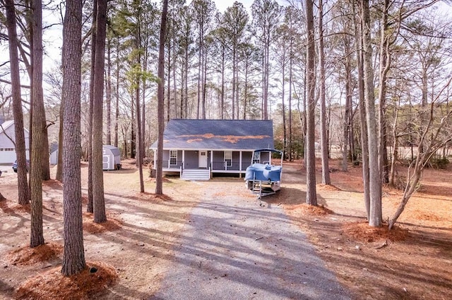 view of front of home with covered porch, driveway, a storage unit, and an outdoor structure