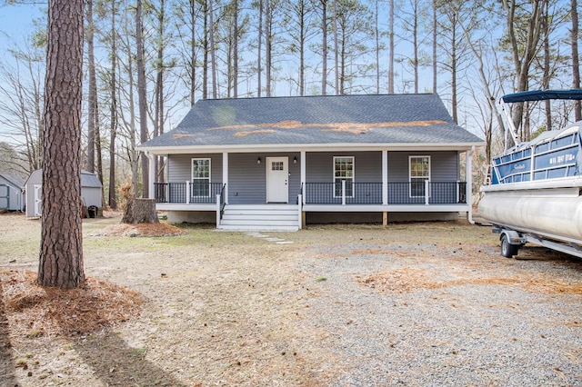 view of front of house featuring an outbuilding, a shed, a porch, and roof with shingles