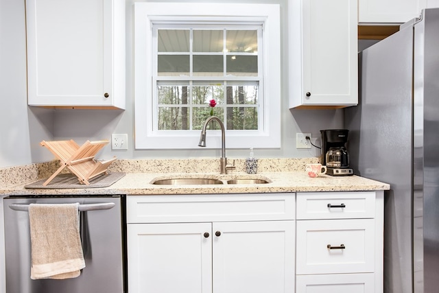 kitchen featuring white cabinets, light stone counters, stainless steel appliances, and a sink