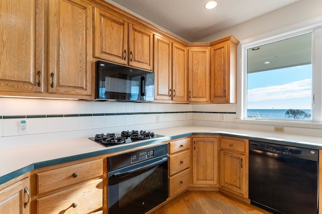 kitchen featuring black appliances, a water view, light wood-type flooring, a textured ceiling, and tasteful backsplash