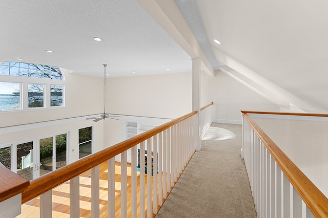 hallway with light carpet, lofted ceiling with beams, and a textured ceiling