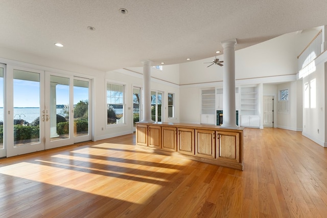 interior space with ornate columns, ceiling fan, a water view, and vaulted ceiling