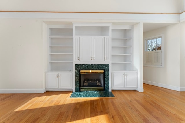 unfurnished living room featuring built in shelves, light hardwood / wood-style floors, and a premium fireplace