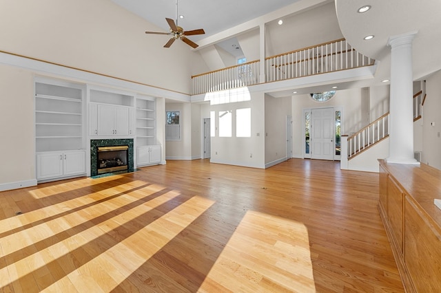 unfurnished living room featuring ceiling fan, light wood-type flooring, built in features, a fireplace, and a towering ceiling